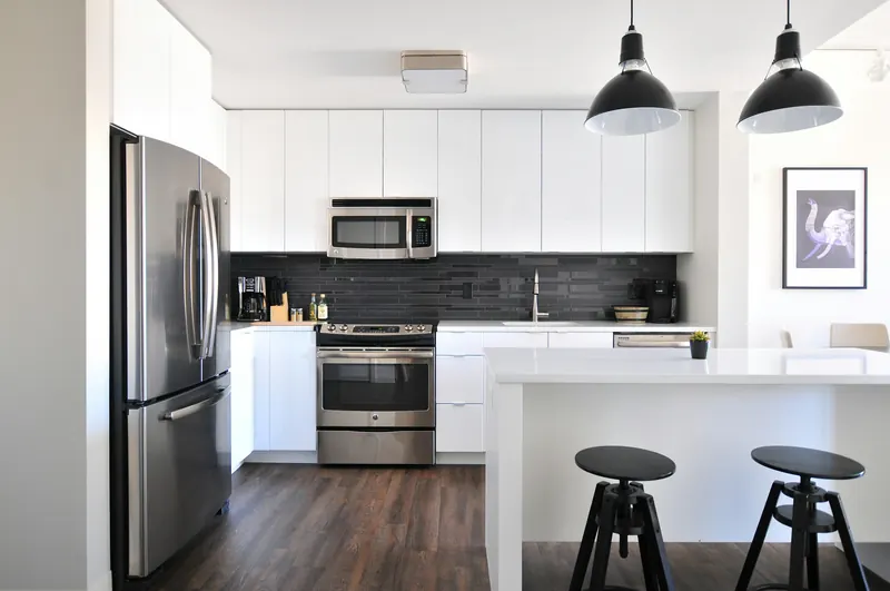 Cocina moderna y luminosa con refrigeradora de acero inoxidable, horno y barra con taburetes