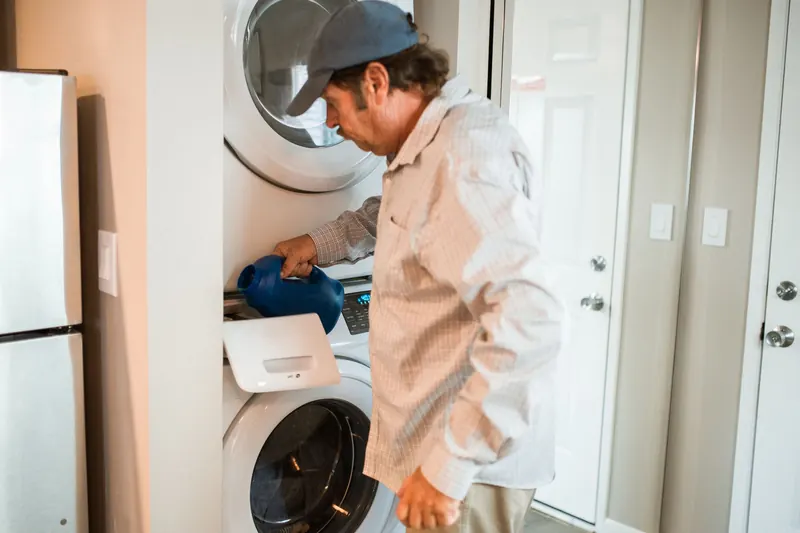 Hombre revisando el cajón de detergente de una lavadora y secadora apiladas en una casa