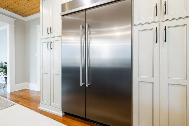 Refrigeradora de acero inoxidable de dos puertas empotrada entre muebles blancos de cocina